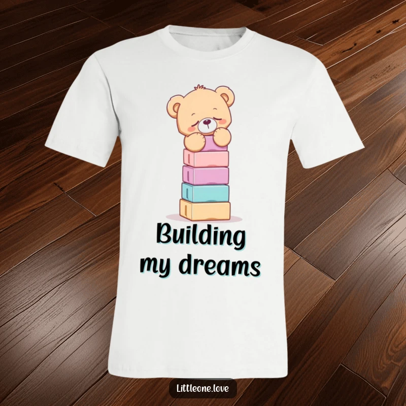 Funny t-shirt featuring a drowsy teddy bear precariously balancing a high stack of blocks, a humorous scene of effort.